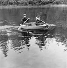Bengt Eckerrot och Mats Lindgren och  paddlar en liten jolle. Mats Lindgren har en flytring runt halsen