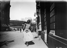 En kvinna bär ett barn längs Tegnérgatan österut mot Roslagstorg. Till höger Tegnérgatan 3 och i fonden Eriksberg.