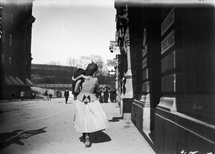 En kvinna bär ett barn längs Tegnérgatan österut mot Roslagstorg. Till höger Tegnérgatan 3 och i fonden Eriksberg.