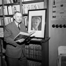 Drottninggatan 62. Interiör från Björck & Börjesson Antikvariat - Bokhandel. En man står med en uppslagen bok invid ett porträtt av August Strindberg