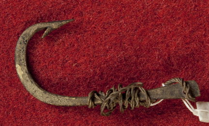 Medeltida metkrok i järn med tafs fotograferad mot röd bakgrund. 