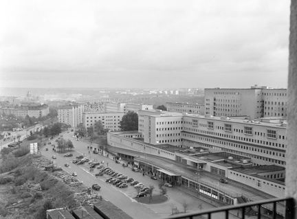 Från en hög byggnad syns ett stort och modernt sjukhuskomplex med flera byggnader och en parkering. 