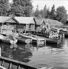 Fiskeläge i Rävsnäs med bryggor och sjöbodar. Scouter med packning på brygga