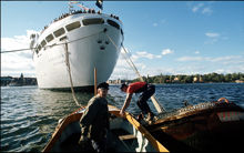 Två män i en liten båt jobbar med bojen vid vilken M/S Kungsholm ligger förtöjd