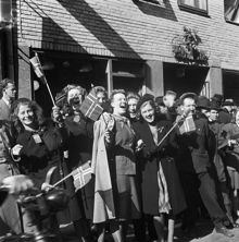 Fredsdagen den 7:e maj 1945. Glada människor viftar med flaggor framför Mäster Samuelsgatan 18.