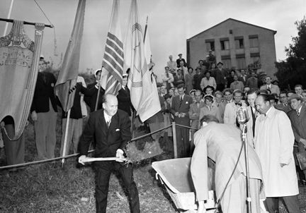 Ministern med spade, skottkärra intill. Fanbärare och publik bakom.