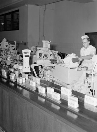 En man står vid ett löpande band och packar olika mjölkprodukter.