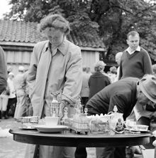 Auktion. Kvinna vid pelarbord med auktionsgods