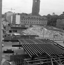 Vy över rivna kvarteret Kajan. Klarabergsviadukten byggs. T.v. Klarabergsgatan och i fonden Klara kyrka och Klara västra kyrkogata. T.h. Klara Vattugränd och i förgrunden Vasagatan
