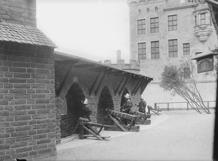 Tegelhus med mur, människor står vid medeltida kanoner