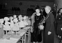 Fridhemsgatan 25. Syföreningsdag på Stockholms stads handelsgymnasium. Prostinnan Greta Hellerström visar drottning Louise av Sverige (Mountbatten) en utställning av handarbetsmodeller