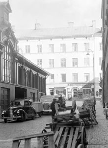 Bilar och dragkärror utanför den gamla Hötorgshallen. I höger kant Nya Elementarskolan, kv. Beridarebanan. I fonden Hötorget 10 (Sergelgatan 10) i kv. Grytgjutaren, nu platsen för första höghuset