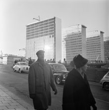 Femte hötorgshuset under färdigställande. Hamngatan mot nuvarande Sergels Torg, där byggnadsarbete pågår. Människor står vid ett plank och tittar ned i gropen
