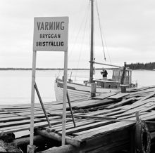 Skuta  förtöjd vid fallfärdig brygga med varningsskylt. I Stockholms norra skärgård