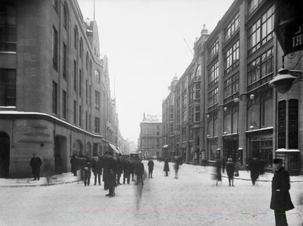 Vy längs Hamngatan österut från korsningen Regeringsgatan. Till vänster varuhuset NK, Nordiska Kompaniet, och till höger Hamngatspalatset med bl.a.varuhuset Sidenhuset
