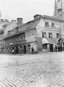 Mäster Samuelsgatan 63 vid hörnet av Vasagatan 26. Klaras kyrkas torn skymtar i högra hörnet. Dåv. kv. Svanen, nuv. kv. Orgelpipan. Nuv. Mäster Samuelsgatan 73